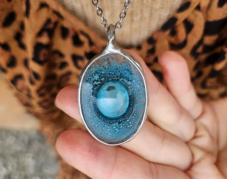 Owalny wisior z turkusowym szklanym  oczkiem (oprawa w kolorze srebrnym)